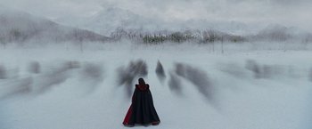 A woman in a black and red cape standing in front of a snowy mountain