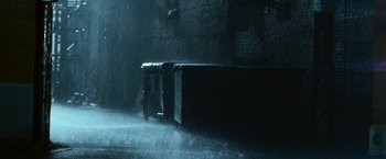 Movie still from “The Twilight Saga: Eclipse” (2010), directed by David Slade – A person standing in the rain next to a brick wall; Wide shot, Low angle