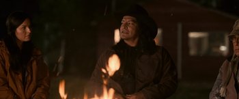 Movie still from “The Twilight Saga: Eclipse” (2010), directed by David Slade – A man wearing a black hat standing in front of a fire; Medium shot, Over the shoulder angle