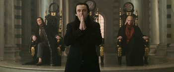 Movie still from “The Twilight Saga: New Moon” (2009), directed by Chris Weitz – A man in a black coat is praying; Medium shot, Low angle