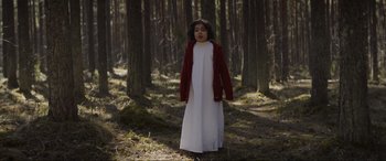 Movie still from “The Twin” (2022), directed by Taneli Mustonen – A young girl in a white dress in the woods; Wide shot, Low angle