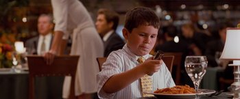 Movie still from “The Ugly Truth” (2009), directed by Robert Luketic – A young boy in a dress shirt and tie eating a plate of food; Medium shot, Over the shoulder angle