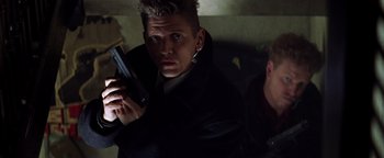 Movie still from “Enemy of the State” (1998), directed by Tony Scott – A man holding a gun while standing next to another man; Close Up shot, Low angle