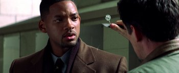 Movie still from “Enemy of the State” (1998), directed by Tony Scott – A man in a brown suit and tie looking at a person in a brown suit; Close Up shot, Over the shoulder angle