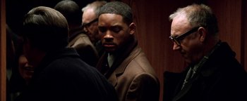 Movie still from “Enemy of the State” (1998), directed by Tony Scott – A man in a brown suit is standing next to another man in a brown suit; Close Up shot, Over the shoulder angle