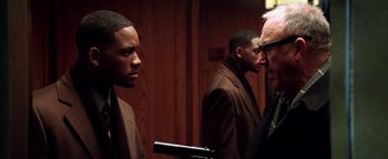 Movie still from “Enemy of the State” (1998), directed by Tony Scott – A group of men standing next to each other in a room; Close Up shot, Over the shoulder angle