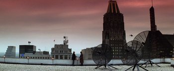 Movie still from “Enemy of the State” (1998), directed by Tony Scott – Two people are standing on a roof top near a fan; Extreme Wide shot, Low angle
