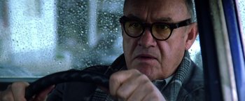 Movie still from “Enemy of the State” (1998), directed by Tony Scott – An older man wearing glasses driving in the rain; Close Up shot, Low angle