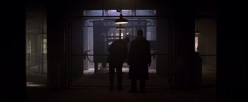 Movie still from “Enemy of the State” (1998), directed by Tony Scott – Two men are standing in the dark in front of an electric fence; Wide shot, Low angle