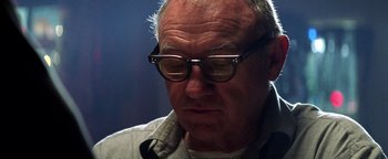 Movie still from “Enemy of the State” (1998), directed by Tony Scott – An older man wearing glasses looking down at his face; Close Up shot, Low angle