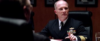 Movie still from “Enemy of the State” (1998), directed by Tony Scott – A man wearing a suit and tie sitting at a table; Close Up shot, Over the shoulder angle