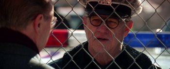 Movie still from “Enemy of the State” (1998), directed by Tony Scott – An older man wearing a police hat and glasses; Close Up shot, Over the shoulder angle