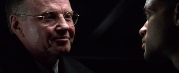 Movie still from “Enemy of the State” (1998), directed by Tony Scott – An older man wearing glasses and wearing a suit; Close Up shot, Over the shoulder angle