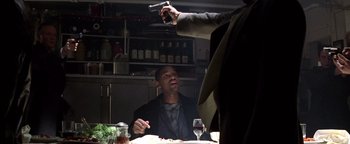 Movie still from “Enemy of the State” (1998), directed by Tony Scott – A man sitting at a dinner table holding a gun up to his face; Medium shot, High angle