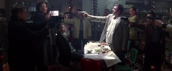 Movie still from “Enemy of the State” (1998), directed by Tony Scott – A man holding a gun pointed at a man sitting at a dinner table; Medium shot, Over the shoulder angle