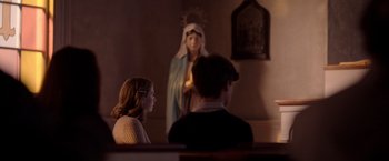 Movie still from “The Unholy” (2021), directed by Evan Spiliotopoulos – A woman and a man sitting in front of a statue of mary; Medium shot, Over the shoulder angle