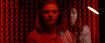 Movie still from “The Unholy” (2021), directed by Evan Spiliotopoulos – A woman wearing headphones in front of a red wall; Close Up shot, Over the shoulder angle