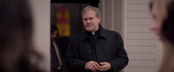 Movie still from “The Unholy” (2021), directed by Evan Spiliotopoulos – A man wearing a black coat standing in front of a building; Close Up shot, Over the shoulder angle