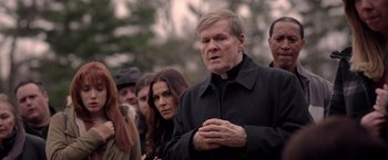Movie still from “The Unholy” (2021), directed by Evan Spiliotopoulos – An older man is standing in front of a group of people; Medium shot, Over the shoulder angle