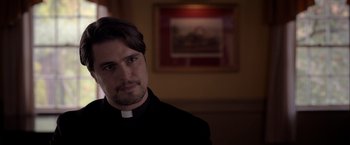 Movie still from “The Unholy” (2021), directed by Evan Spiliotopoulos – A man wearing a priest's outfit in front of a painting; Close Up shot, Low angle