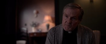 Movie still from “The Unholy” (2021), directed by Evan Spiliotopoulos – An older man wearing a priest's collar; Close Up shot, Over the shoulder angle