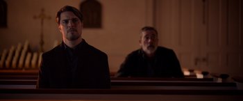 Movie still from “The Unholy” (2021), directed by Evan Spiliotopoulos – Two men sitting in a church pews looking at each other; Medium shot, Over the shoulder angle