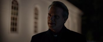 Movie still from “The Unholy” (2021), directed by Evan Spiliotopoulos – A man wearing a priest's collar and a white shirt; Close Up shot, Low angle