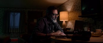 Movie still from “The Unholy” (2021), directed by Evan Spiliotopoulos – A man sitting at a table in a dark room; Close Up shot, Over the shoulder angle