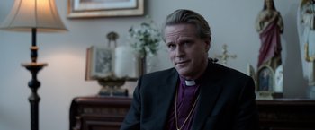 Movie still from “The Unholy” (2021), directed by Evan Spiliotopoulos – A man wearing a suit and a priest's collar; Close Up shot, Over the shoulder angle