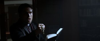 Movie still from “The Unholy” (2021), directed by Evan Spiliotopoulos – A man in a black suit holding a rosary and a book; Close Up shot, Over the shoulder angle