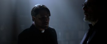Movie still from “The Unholy” (2021), directed by Evan Spiliotopoulos – A man with a priest's collar is standing in the dark; Close Up shot, Low angle