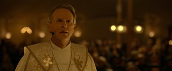 Movie still from “The Unholy” (2021), directed by Evan Spiliotopoulos – A man wearing a priest's outfit with a microphone in front of a group of people; Close Up shot, Low angle