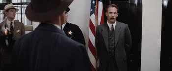 Movie still from “The Untouchables” (1987), directed by Brian De Palma – A man in a suit standing next to an american flag; Medium shot, Over the shoulder angle