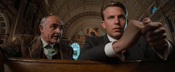 Movie still from “The Untouchables” (1987), directed by Brian De Palma – Two men sitting at a table in front of a painting; Medium shot, Low angle