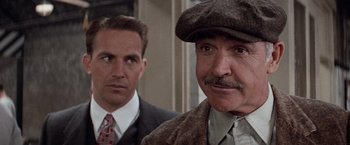 Movie still from “The Untouchables” (1987), directed by Brian De Palma – A man in a hat and tie next to another man in a suit and tie; Close Up shot, Over the shoulder angle