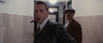 Movie still from “The Untouchables” (1987), directed by Brian De Palma – A man smoking a cigar while another man looks on; Close Up shot, Low angle