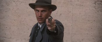 Movie still from “The Untouchables” (1987), directed by Brian De Palma – A man in a hat and a suit points a gun; Close Up shot, Low angle