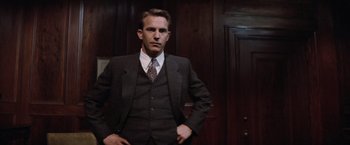 Movie still from “The Untouchables” (1987), directed by Brian De Palma – A man in a suit and tie standing in front of a wooden wall; Medium shot, Low angle