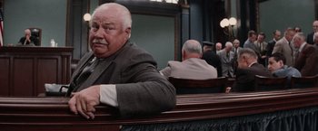 Movie still from “The Untouchables” (1987), directed by Brian De Palma – An older man sitting in a courtroom with other people; Medium shot, Over the shoulder angle
