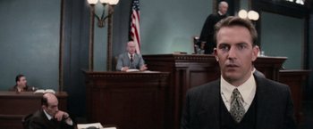 Movie still from “The Untouchables” (1987), directed by Brian De Palma – A man in a suit sitting in front of a judge in a courtroom; Medium shot, Over the shoulder angle