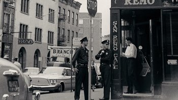Movie still from “The Velvet Underground” (2021), directed by Todd Haynes – Two police officers standing on a street corner; Wide shot, Low angle