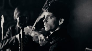 Movie still from “The Velvet Underground” (2021), directed by Todd Haynes – A man holding a microphone and a microphone stand; Close Up shot, Low angle