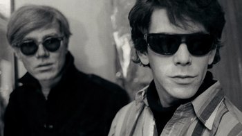 Movie still from “The Velvet Underground” (2021), directed by Todd Haynes – A man wearing sunglasses standing next to another man; Close Up shot, Low angle