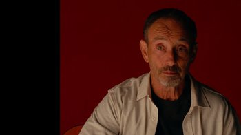 Movie still from “The Velvet Underground” (2021), directed by Todd Haynes – An older man sitting in front of a red wall; Close Up shot, Low angle