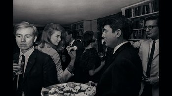 Movie still from “The Velvet Underground” (2021), directed by Todd Haynes – A man and a woman standing next to each other at a party; Medium shot, Low angle