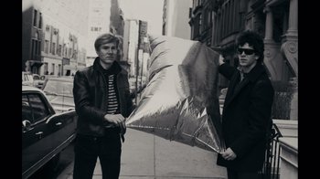 Movie still from “The Velvet Underground” (2021), directed by Todd Haynes – Two young men standing on the side of the street holding a large umbrella; Medium shot, Low angle