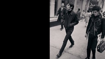 Movie still from “The Velvet Underground” (2021), directed by Todd Haynes – A man walking down the street in a black jacket; Medium shot, Low angle