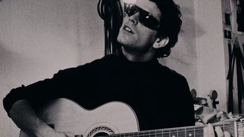 Movie still from “The Velvet Underground” (2021), directed by Todd Haynes – A man in sunglasses playing an acoustic guitar; Close Up shot, Low angle