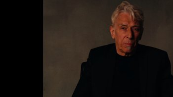 Movie still from “The Velvet Underground” (2021), directed by Todd Haynes – An older man in a black suit is posing for a picture; Close Up shot, Low angle