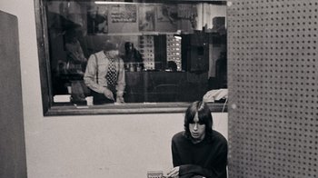 Movie still from “The Velvet Underground” (2021), directed by Todd Haynes – A person sitting in front of a store window; Medium shot, High angle